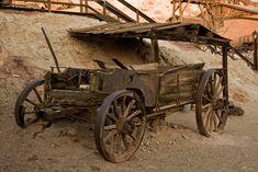 an old wooden cart sitting on top of a dirt hill next to a building and stairs