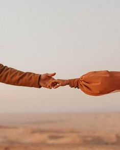 two people holding hands and touching each other in front of a desert landscape with no clouds