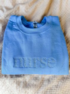 a blue shirt with the word bliss embroidered on it sitting on top of a bed