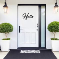 a white door with two potted plants on the side and a hello sign above it