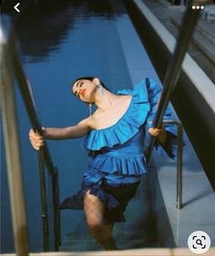 a woman in blue dress leaning on railing