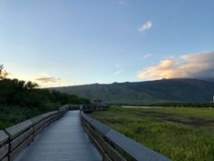 a wooden walkway in the middle of a grassy field with mountains in the background at sunset