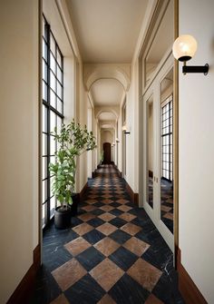 a long hallway with black and white checkered flooring, potted plant on the far end