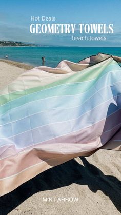 there is a blanket on the beach with people in the water and sand behind it