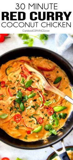 a pan filled with red curry and vegetables on top of a white table next to a spoon