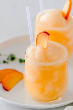 two glasses filled with orange juice and garnished with peach slices on a white plate