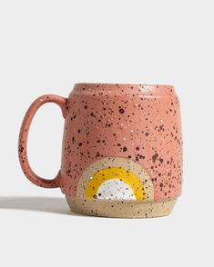 a pink and yellow coffee mug with black speckles on the outside, in front of a white background