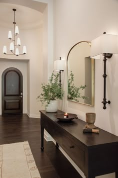 a hallway with a table, mirror and plant on it's sideboard in front of a doorway