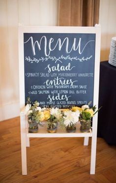 a chalkboard sign with flowers on it sitting in front of a table that has a menu written on it