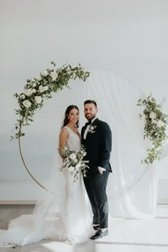 a bride and groom standing in front of an arch with greenery