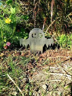 a metal ghost sitting in the middle of some grass and flowers with its eyes open