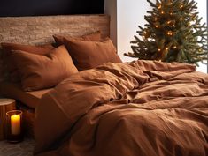 a bed with brown sheets and pillows next to a lit christmas tree