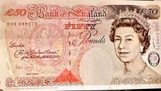 an old british fifty pound note is being held up by someone's hand in front of the camera