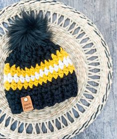 a black and yellow knitted hat on top of a white wicker basket with a leather tag