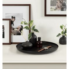 there is a black plate with some plants in it and pictures on the wall behind it