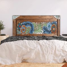 a bed with white sheets and blue flowers painted on the headboard, in a bedroom