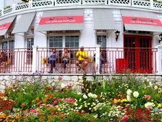 people standing on the balcony of a building with flowers in front of it and red doors