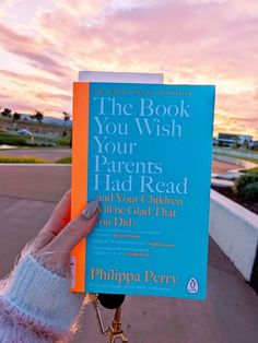 the book you wish your parents had read is held up in front of a sunset