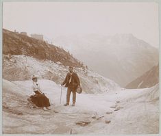 an old photo of two people standing in the snow with mountains in the back ground