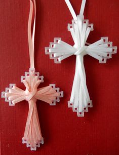 two cross ornaments are hanging on a red wall next to each other, one is white and the other has pink ribbon