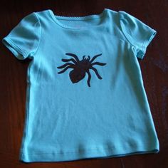 a blue t - shirt with a black spider on it's chest sitting on a wooden floor