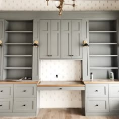 an empty kitchen with gray cabinets and wood flooring on the walls, in front of a chandelier