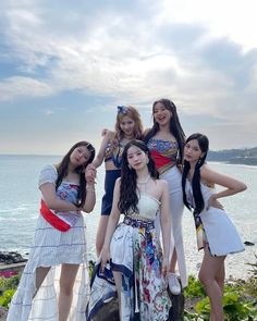 four young women standing next to each other in front of the ocean