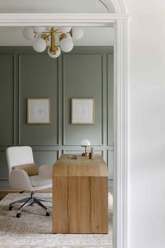 an office with a desk and chair in front of green paneled walls, along with two framed pictures on the wall