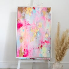 an abstract painting with pink, yellow and blue colors is displayed on a easel