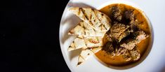 a white plate topped with meat and tortilla chips next to a bowl of soup