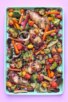 a blue tray filled with chicken, vegetables and broccoli on top of a pink surface