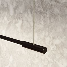 a black object hanging from a chain on a marble wall with white and gray colors