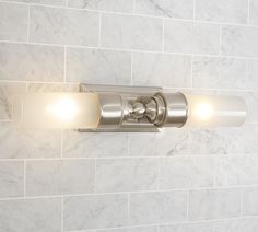 a bathroom light that is on the side of a brick wall in a white tiled room