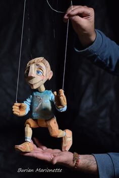 a hand holding a wooden doll hanging from strings