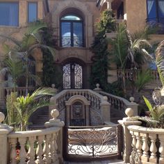 the entrance to a large house with plants on either side and an iron gate in front