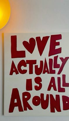 a red and white sign that says love actually is all around on the wall next to a lamp