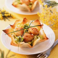 two white plates with food on them sitting on a table next to yellow flowers and silverware