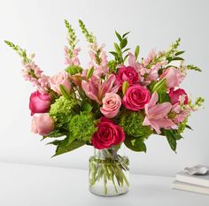 a vase filled with lots of pink and red flowers on top of a wooden table