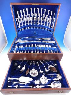 an assortment of silverware in a wooden box with blue velvet lining and matching handles