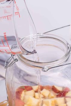 someone pouring liquid into a glass jar filled with fruit