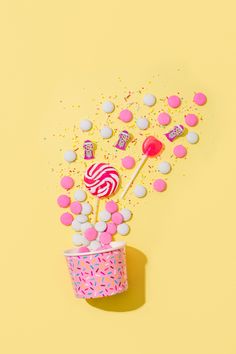 a cup filled with candy and lollipops on top of a yellow background