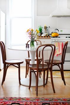 a kitchen table with four chairs and a vase filled with flowers on top of it