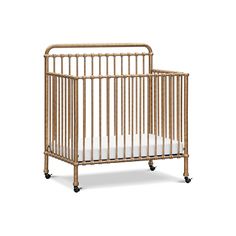 a baby crib with white sheets on the bottom and wheels in front of it