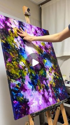 a woman is painting on an easel with purple and green colors in the background