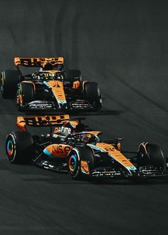 three racing cars driving on a track during the night time, one is orange and blue