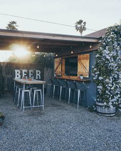 an outdoor bar with several stools and tables in front of it, surrounded by greenery