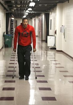 a man walking down a hallway with crutches in his hand and wearing a red sweatshirt