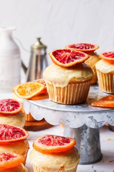 orange muffins with icing and blood orange slices on top, sitting on a cake stand