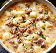 a white bowl filled with meat and cheese soup on top of a wooden cutting board