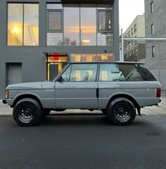 an old grey car parked in front of a tall building with windows on the side